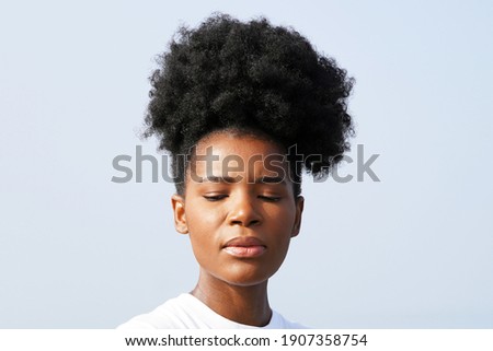 Beautiful young black woman with gorgeous skin and an updo afro pony tail stands against the blue sky outside for a closeup portrait                               