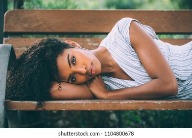 Beautiful Young Black Woman Laying Down On A Chair In A Park