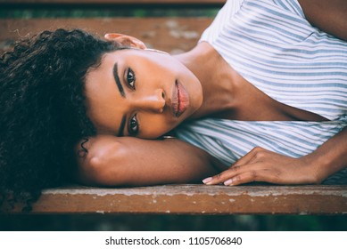 Beautiful Young Black Woman Laying Down On A Chair In A Park