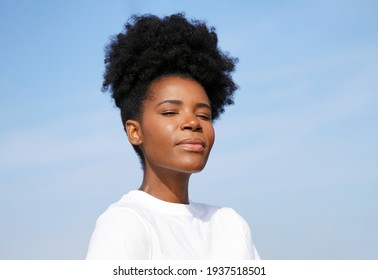 Beautiful young black woman looks forward against a blue sky for a closeup portrait outside on a clear day                               