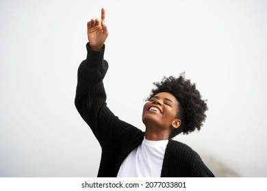 Beautiful young black woman points up to the heavens and god with her eyes closed and smiling outside in the fog at the ocean                                - Shutterstock ID 2077033801