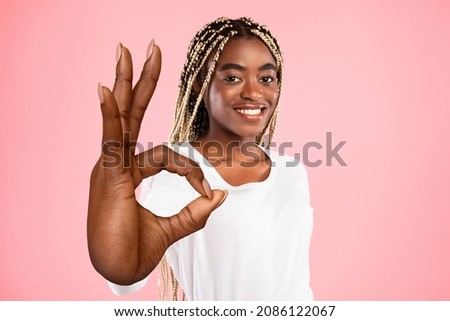 Beautiful young black woman showing big OKAY gesture on pink studio background. Lovely African American female expressing her approval or support, giving positive feedback
