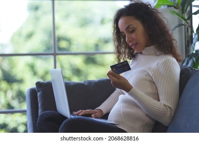 Beautiful Young Black Woman Smiling And Using Laptop And Credit Card For Shopping Online On Sofa At Home. Business Woman And Freelance Work From Home In Spreading Of Coronavirus Covid-19.