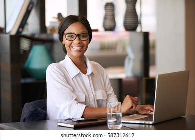 Beautiful young black woman smiling at camera while seated behind her personal computer, where she was working on managing her finances for the upcoming tax period and making online payments.