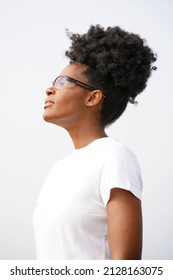 Beautiful young black woman stands outside on a foggy day wearing a short sleeved white shirt, sporty glasses and an updo afro high puff hairstyle looking left                              