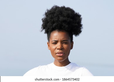 Beautiful Young Black Woman With Updo High Puff Hairstyle Stands At The Ocean And Looks Forward For A Closeup Portrait Of Her Face And Shoulders                           