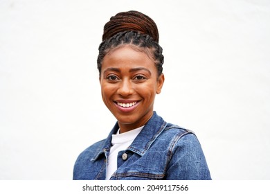 Beautiful Young Black Woman Wearing A Jeans Jacket And Braided Updo Bun Hairstyle Looks Forward And Smiles                               