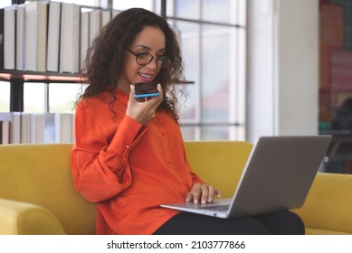 Beautiful Young Black Woman Wearing Orange Shirt Using Laptop And Smartphone For Communication On Sofa At Home. Business Woman And Freelance Work From Home In Spreading Of Coronavirus Covid-19.