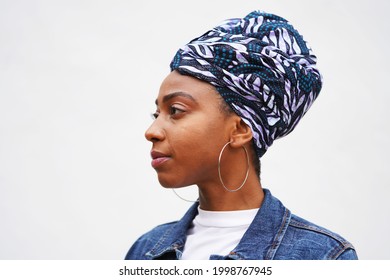 Beautiful Young Black Woman Wears A Patterned Turban And Jeans Jacket For A Profile Portrait With Silver Hoop Earrings                               