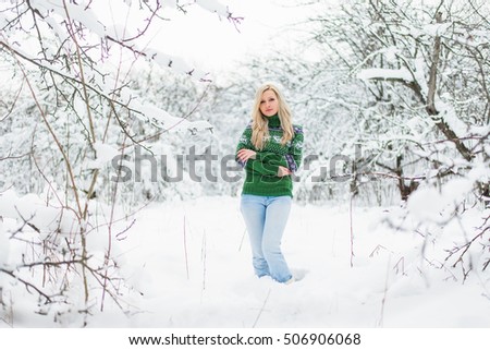 Beautiful young blond hair woman is dressed in a warm green sweater with norwegian patterns on the snowy background in the winter forest. Christmas theme