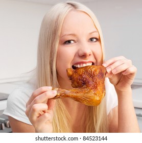 Beautiful Young Blond Woman Eating Chicken In The Kitchen At Home