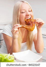 Beautiful Young Blond Woman Eating Chicken In The Kitchen At Home