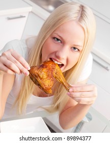 Beautiful Young Blond Woman Eating Chicken In The Kitchen At Home