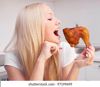 Beautiful Young Blond Woman Eating Chicken In The Kitchen At Home