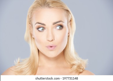 Beautiful young blond woman with an excited look of anticipation making a moue with her mouth and raising her eyebrows as she glances to the right of the frame
