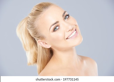 Beautiful young blond woman with her hair in a ponytail posing with bare shoulders and her head tilted back smiling at the camera