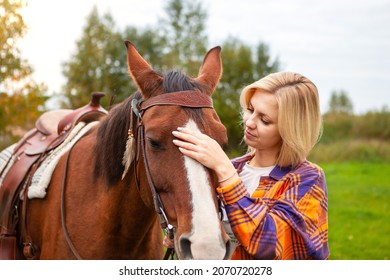 Beautiful Young Blond Woman With A Horse. She Looks At Her Horse, Strokes, Hugs And Enjoys It. The Concept Of Love For Nature, Human Interaction With Nature And Animals.