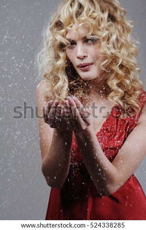 Beautiful young blond woman with perfect makeup and hair in red elegant dress blowing snow and smiling