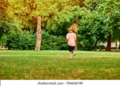 A Beautiful Young Blond Woman Running Away From The Camera Through A Field In A Park
