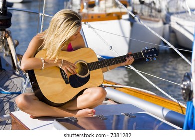 A Beautiful Young Blond Woman Sitting On The Deck Of A Boat Playing Her Guitar