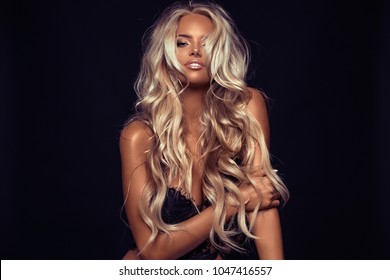 Beautiful young blond woman with wavy long hair posing in the studio on the black background
