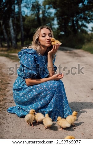 Beautiful young blonde in a blue dress in the woods with ducklings