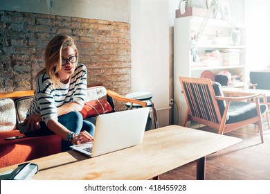 Beautiful Young Blonde Female Student Using Portable Laptop Computer While Sitting In A Vintage Coffee Shop.Young Beautiful Girl Using A Personal Laptop Computer To Look Up Information On The Internet