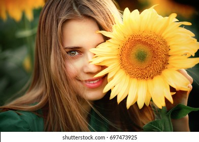 Beautiful young blonde girl in green dress enjoying nature . Happy Smiling female standing in sunflowers field. Warm photo. Art work. - Powered by Shutterstock