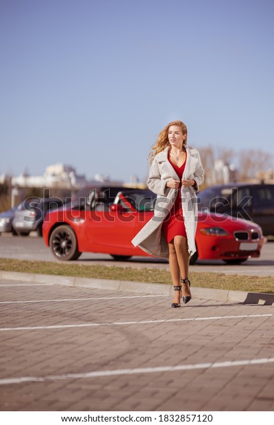 Beautiful young blonde girl in a red dress\
posing in a red car in the city on a sunny\
day