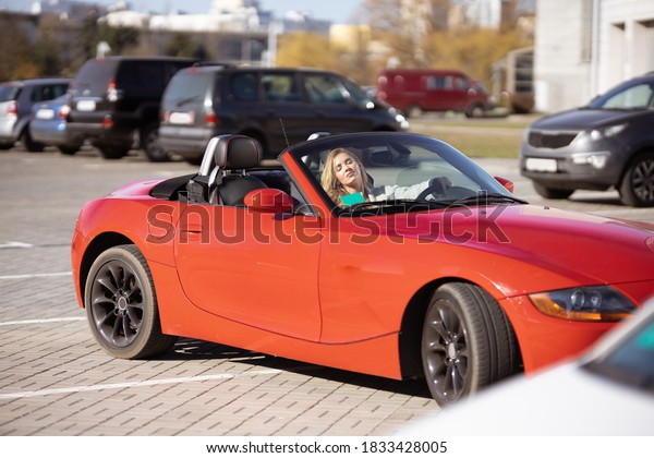 Beautiful young blonde girl in a red dress\
posing in a red car in the city on a sunny\
day