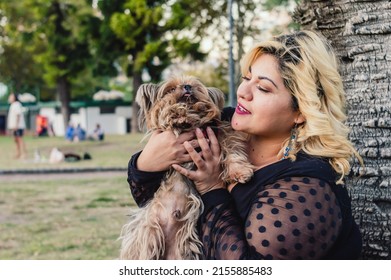 beautiful young blonde plus size woman sitting in the park, leaning against a palm tree, holding and playing with a yorkshire dog.