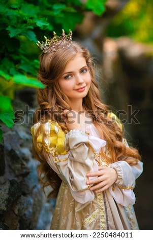Beautiful young blonde princess in gold medieval dress and little crown. Pretty queen posing near stone castle.Warm art work.