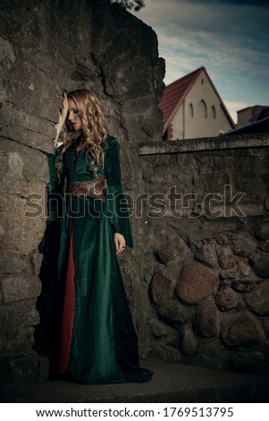 Beautiful young blonde sad girl in the medieval green dress turned away. The legends of Camelot and Lady Guinevere.