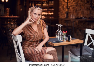 Beautiful young blonde smiling woman sitting in cafe and drinking coffee. Outdoor wine house