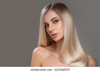Beautiful young blonde with straight shiny hair. Portrait on a gray background. Hair and makeup