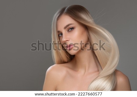 Beautiful young blonde with straight shiny hair. Portrait on a gray background. Hair and makeup