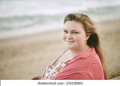 beautiful young Blonde teenage girl smiling at the camera while standing on the beach, with the shoreline in the background