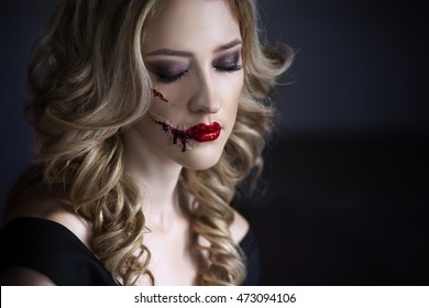 Beautiful young blonde woman in black dress with halloween make up and bloody face art, victim of domestic violence, close up portrait