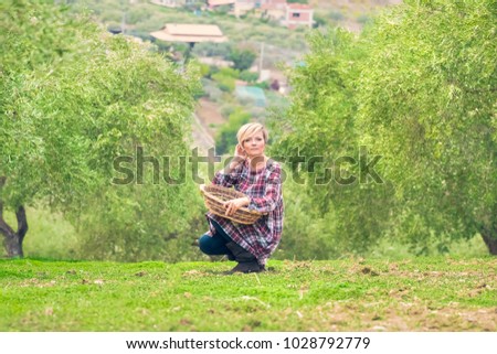 Beautiful young blonde woman in a checkered dress sits with a wicker basket in the summer garden