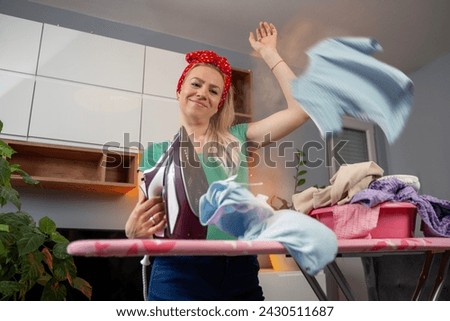Beautiful young blonde woman with cute bow ironing at home, clothes flying around, photomanipulation 
