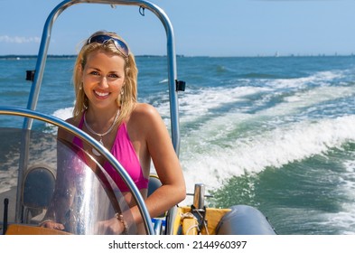 Beautiful young blonde woman girl driving a speedboat on a blue sea in summer sunshine