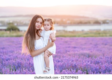 Beautiful Young Blonde Woman Holding Baby Girl Stand In Blooming Lavender Flower Field Outdoor Together. Motherhood. Summer Season. Looking At Camera. Maternity.