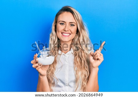 Beautiful young blonde woman holding bowl with sugar surprised with an idea or question pointing finger with happy face, number one 
