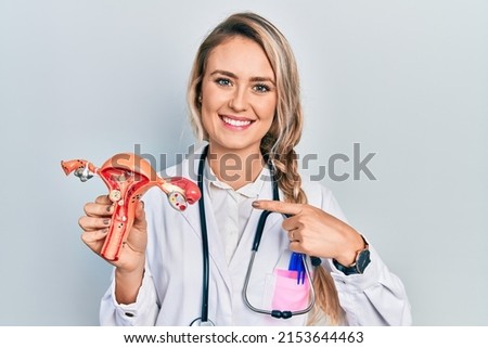 Beautiful young blonde woman holding anatomical model of female genital organ smiling happy pointing with hand and finger 