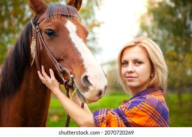 A Beautiful Young Blonde Woman Hugs Her Horse And Looks Into The Camera. The Concept Of Love For Nature, Human Interaction With Nature And Animals.