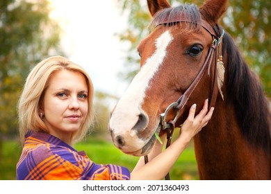 A Beautiful Young Blonde Woman Hugs Her Horse And Looks Into The Camera. The Concept Of Love For Nature, Human Interaction With Nature And Animals.