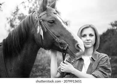 A Beautiful Young Blonde Woman Hugs Her Horse And Looks Into The Camera. The Concept Of Love For Nature, Human Interaction With Nature And Animals.