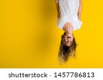 Beautiful young blonde woman jumping happy and excited hanging upside down over isolated yellow background