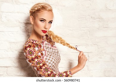 Beautiful Young Blonde Woman In Nice Spring Dress, Posing On White Brick Wall. Fashion Photo, Folklore Style. Braid Hair Style