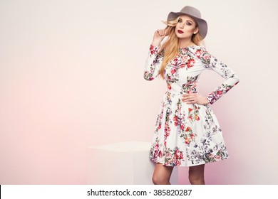 Beautiful Young Blonde Woman In Nice Spring Dress, Hat And Holding A Handbag Posing  In Studio. Fashion Photo